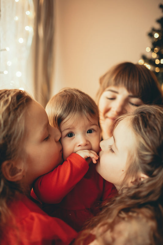 a woman and two children kissing each other in front of a christmas tree