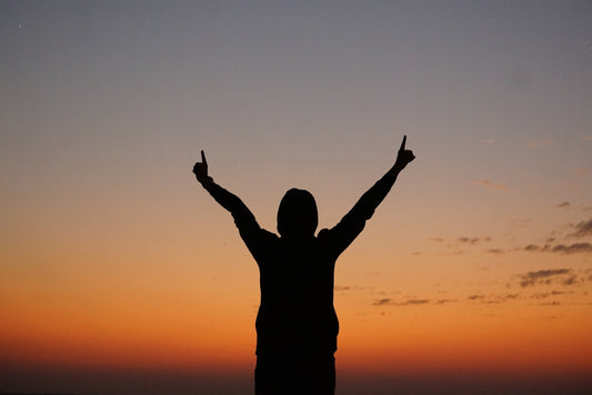 a person with their arms in the air at sunset