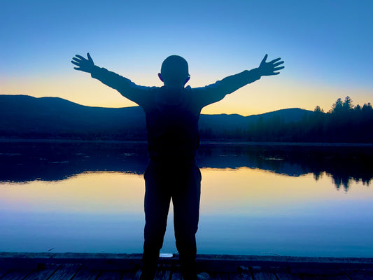 Person stands with arms outstretched at sunset.