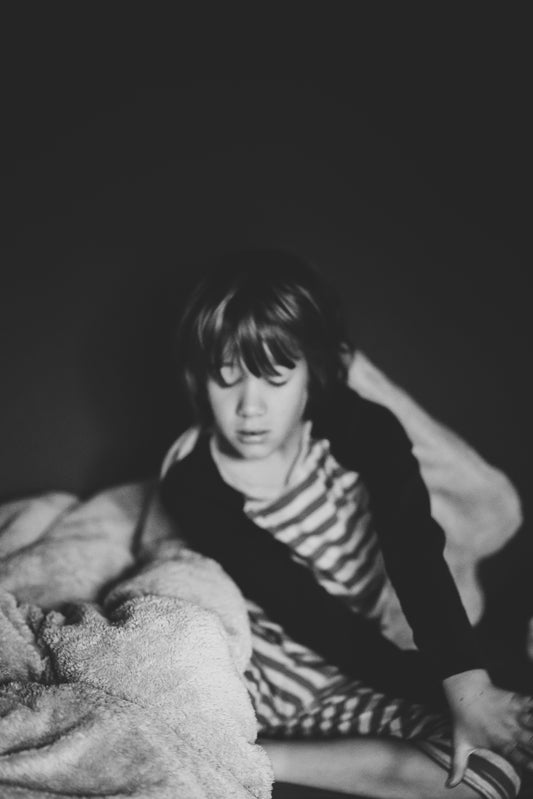 child sitting beside blanket grayscale photo