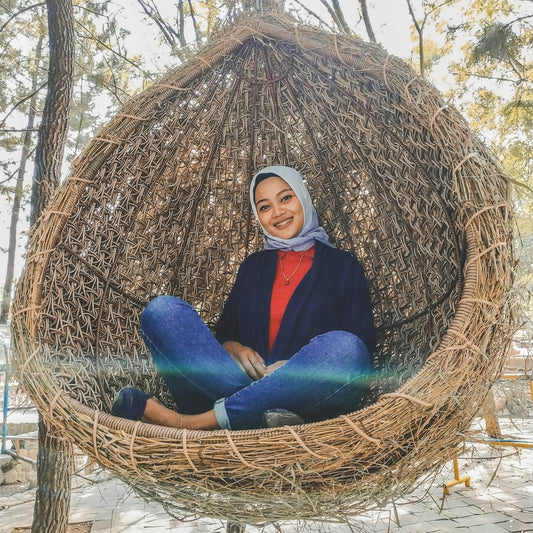 woman sitting on grass wicker egg-shaped swing