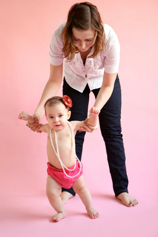 barefooted woman standing and assisting baby while walking