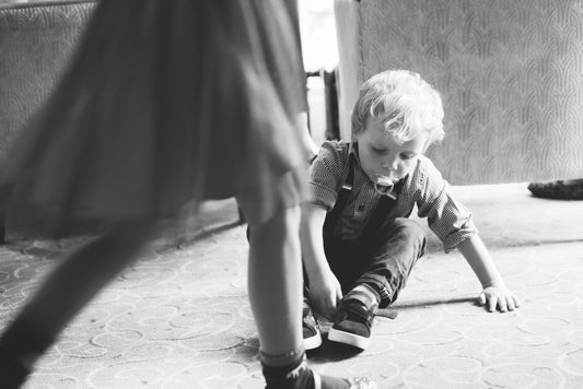 grayscale photography of child with pacifier sitting on floor and another person walking