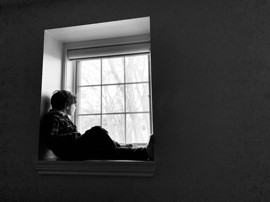 grayscale photo of man and woman sitting beside window