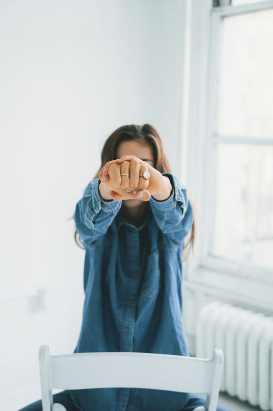 woman in blue denim jacket covering her face with her hands