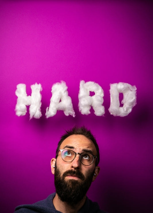 a man with glasses and a beard standing in front of a purple wall with the