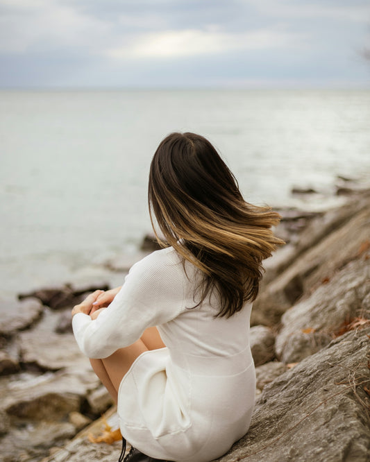 a woman sitting on top of a rock next to the ocean