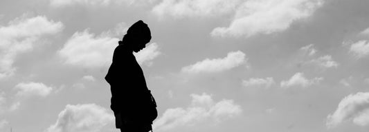 a black and white photo of a person standing in front of a cloudy sky