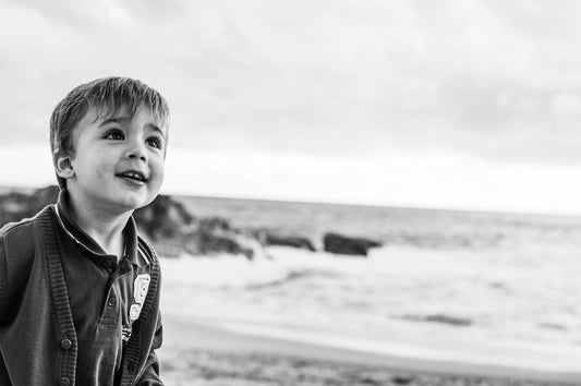 a young boy standing on top of a beach next to the ocean