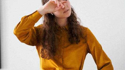 a woman in a yellow shirt is holding her hand up to her face