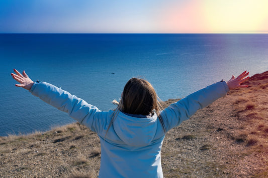 a woman standing on top of a hill next to the ocean