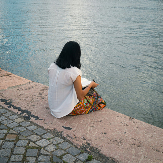 a woman sitting by the water looking at her cell phone