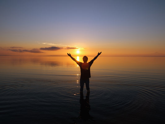 a person standing in the water at sunset