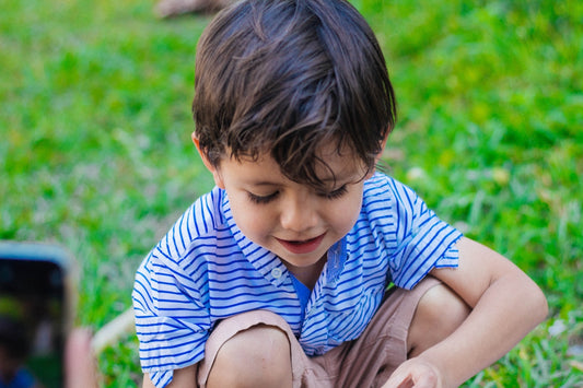 a little boy sitting on the ground playing with a cell phone