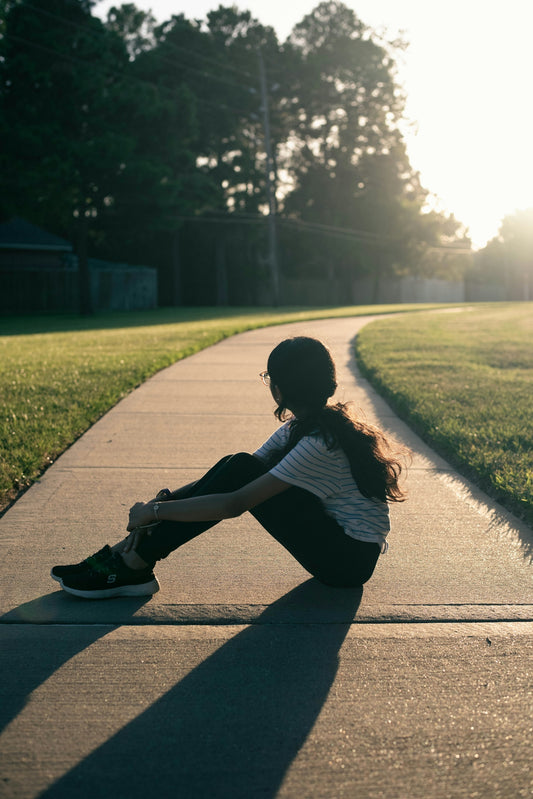 A woman sitting on a sidewalk in the middle of a park