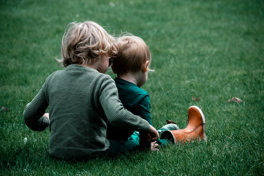 Two children sitting on the grass playing with each other