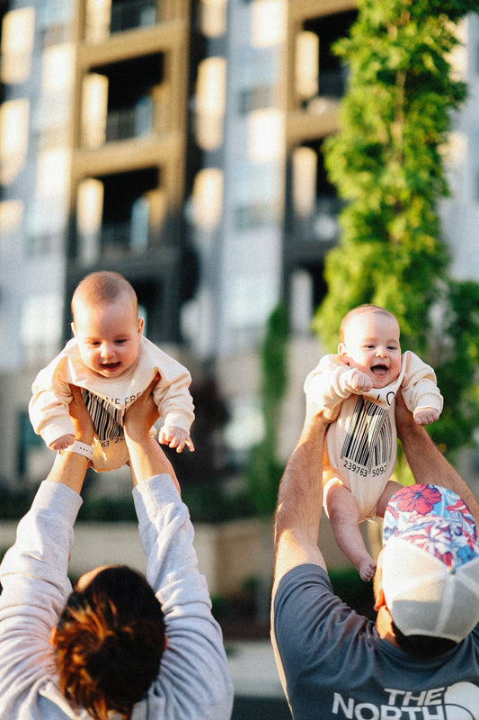 Parents joyfully lift their twin babies in the air.