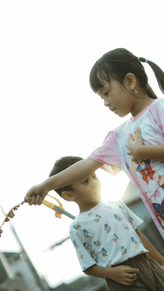 A girl holds a stick over a boy.