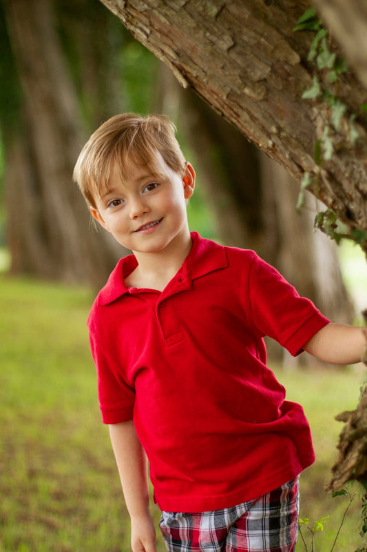 A smiling boy poses near a tree.