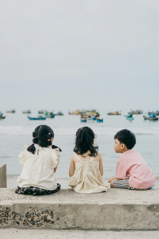 Three children sit and gaze at the sea.