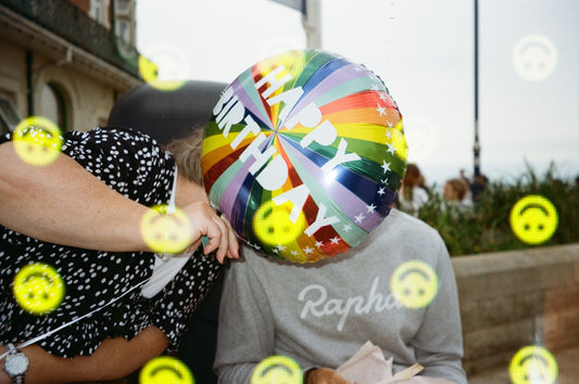 Person with rainbow balloon covering face outdoors