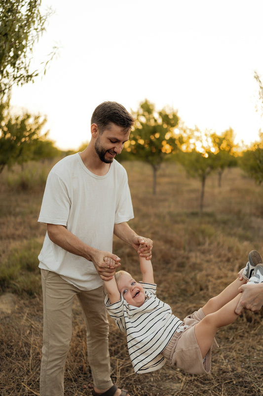 Father swinging happy child in an orchard