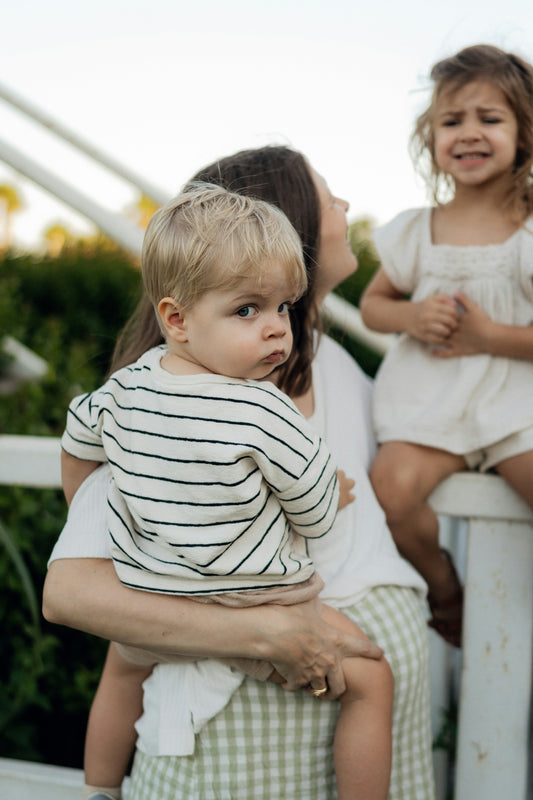 Mother holding a toddler with a girl behind them