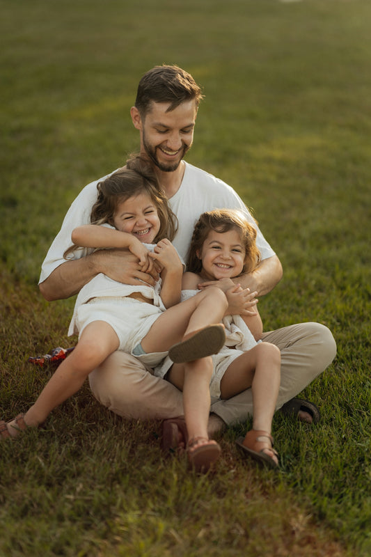 Father smiling with two laughing daughters on grass