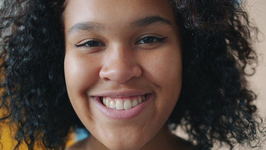 A young woman with curly hair smiles widely smiling.