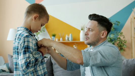 Father helps his son button his shirt