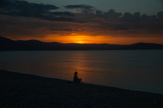 Silhouette of person watching sunset over calm water
