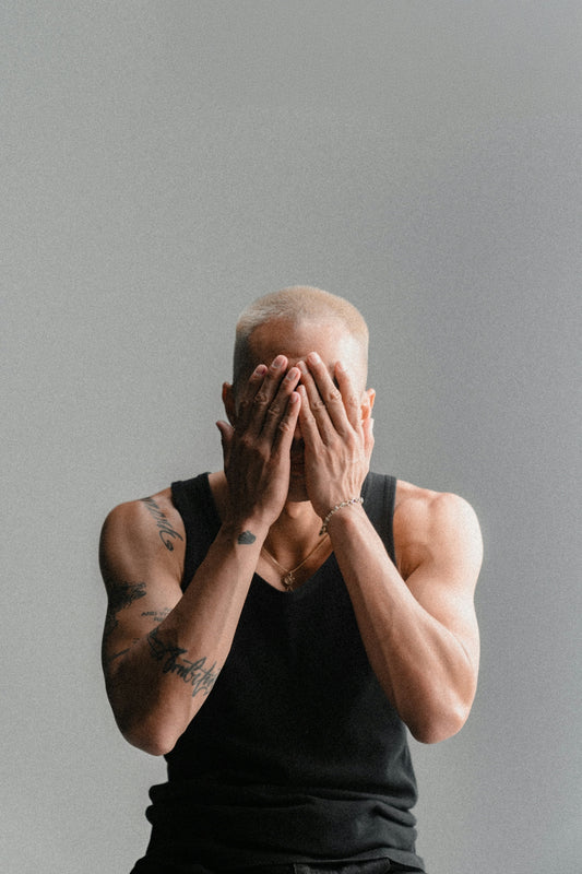 Man covering face with hands against gray background