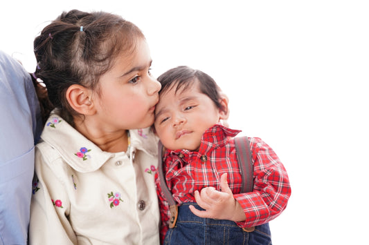 Older sister kisses baby brother on forehead.