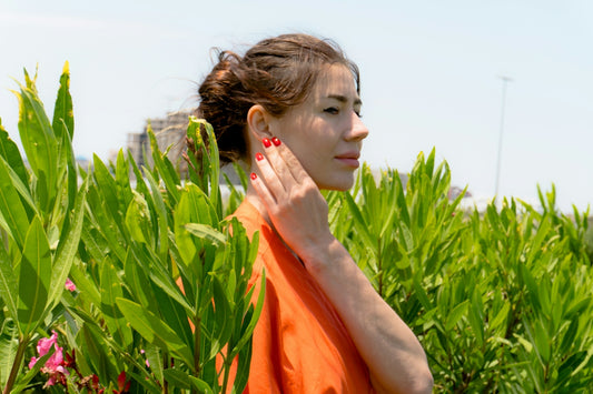 Woman in orange shirt touching her neck amidst greenery