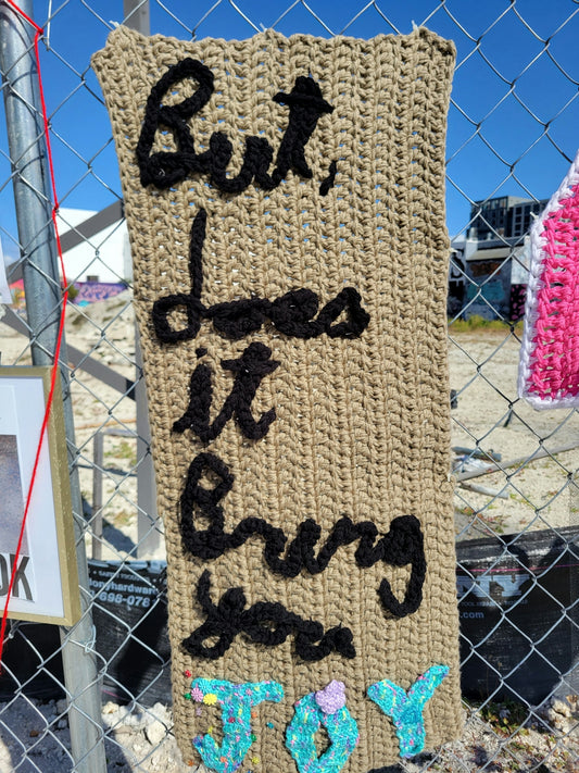 Crocheted sign asking 'but does it bring you joy?'