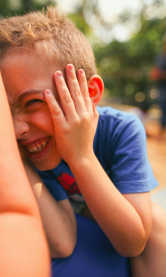 A young boy laughs while covering his face.