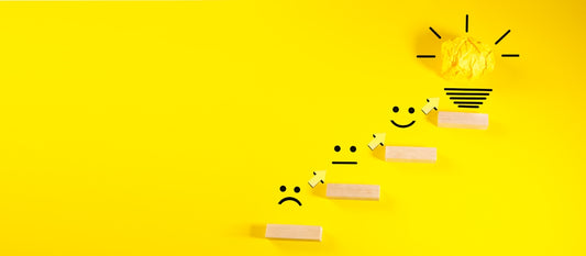 Wooden blocks with smiley faces ascending towards a lightbulb.