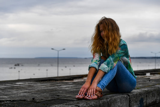 A young woman sits on a ledge overlooking the water.