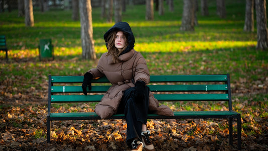 Woman in a hooded coat sits on a park bench.