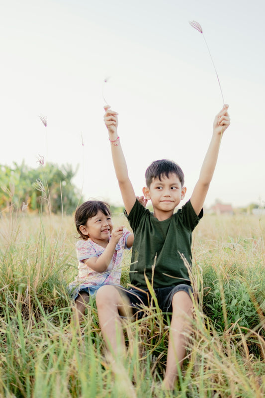 Two children playing with grass in a sunny field
