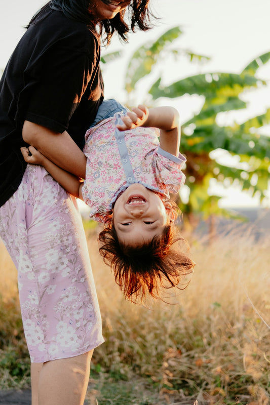 Smiling child held upside down by woman in golden light.