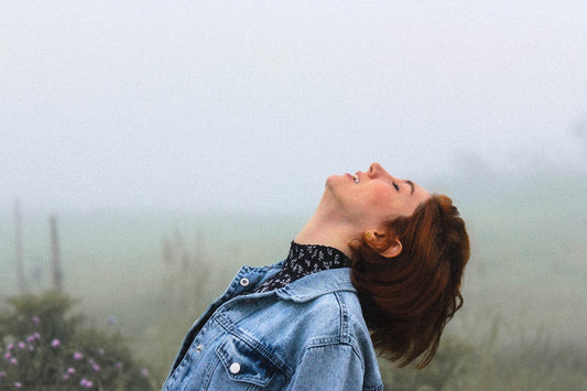 Smiling woman looks up outdoors amidst a foggy background.