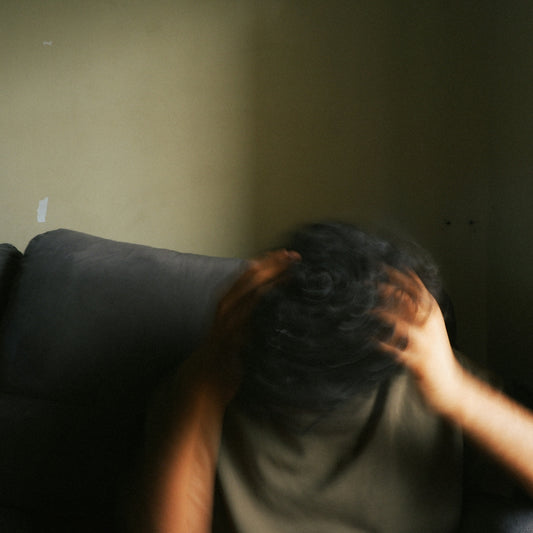 A person with blurred hands touching their head in a dimly lit room