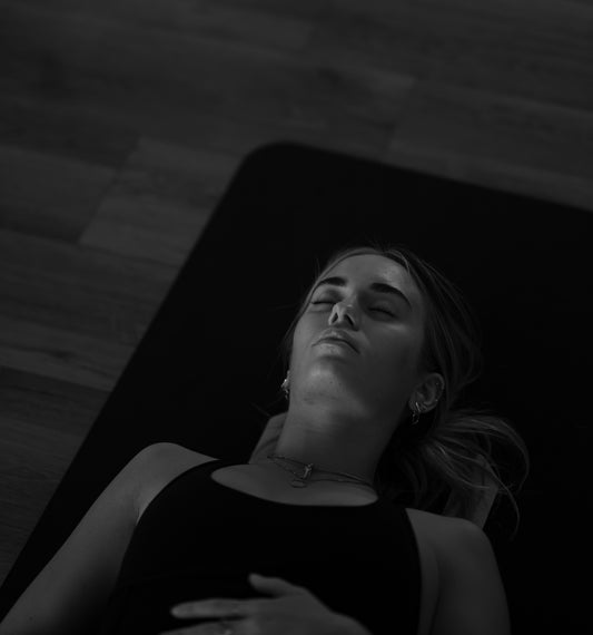 A woman with closed eyes lying on a black yoga mat